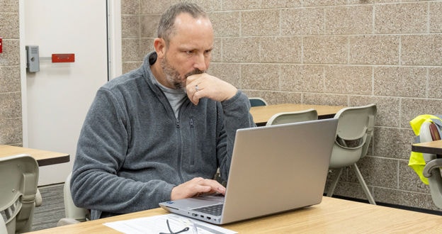 Man sitting in workroom looking at laptop screen contemplating what's on the screen
